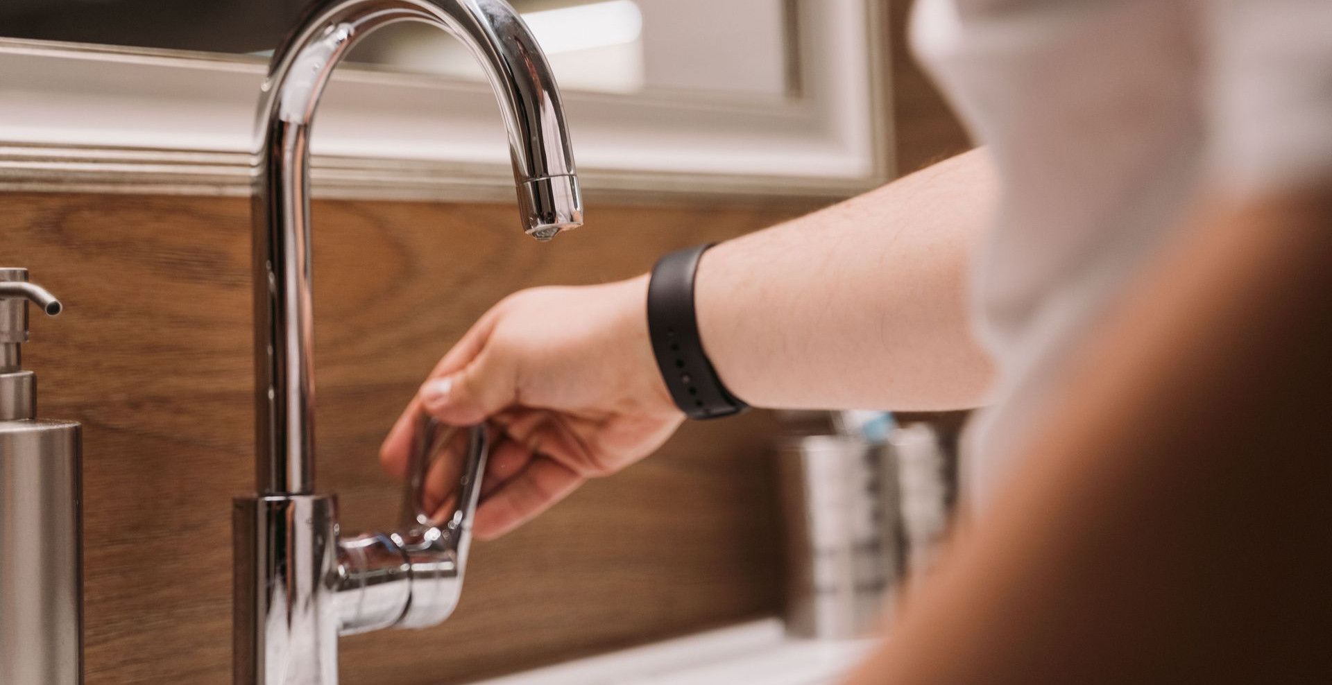 Close-up of a person's hand turning a chrome faucet handle in a modern bathroom setting.
