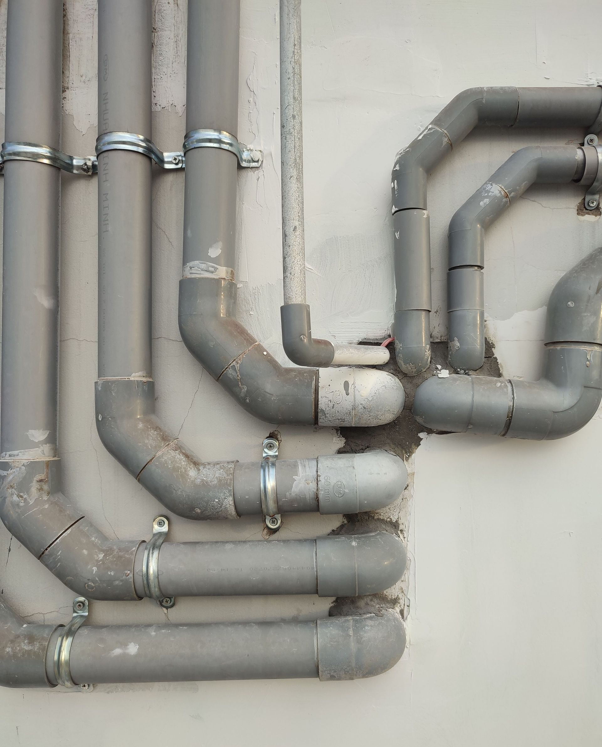 Close-up of interconnected gray metal pipes on an outdoor wall showcasing industrial design.