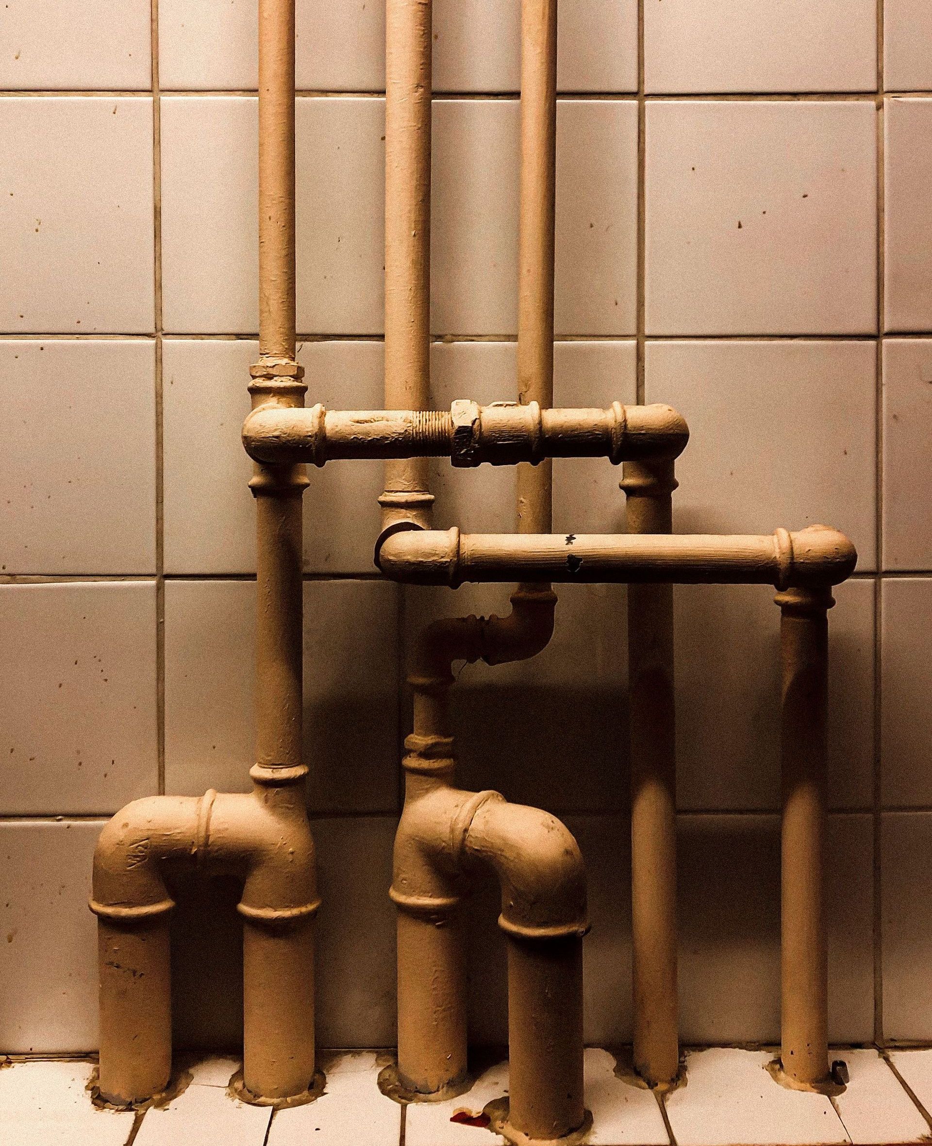 An artistic capture of vertical industrial pipes against a tiled wall, showcasing geometry.