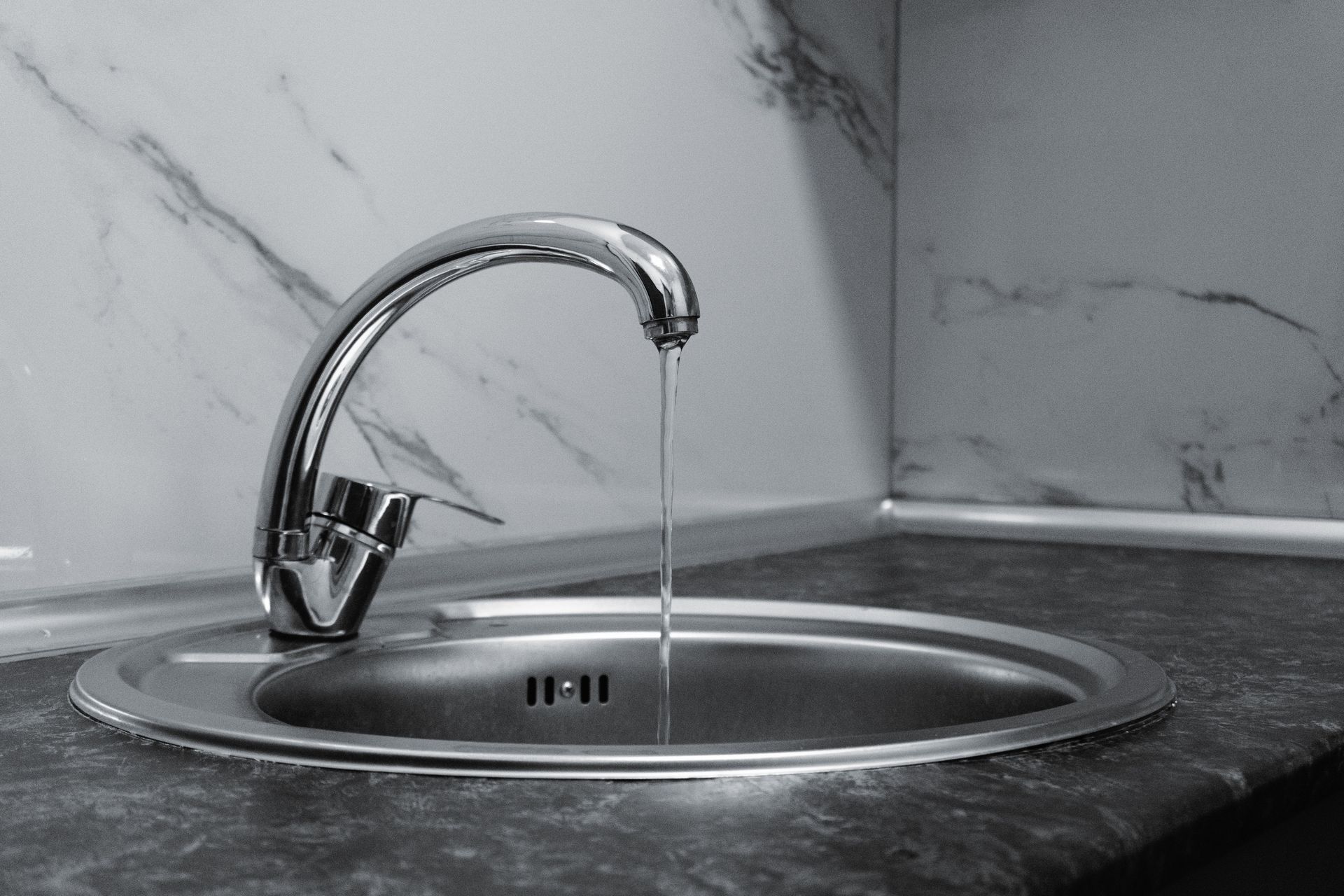 Chrome faucet with running water in a modern kitchen with marble countertop.