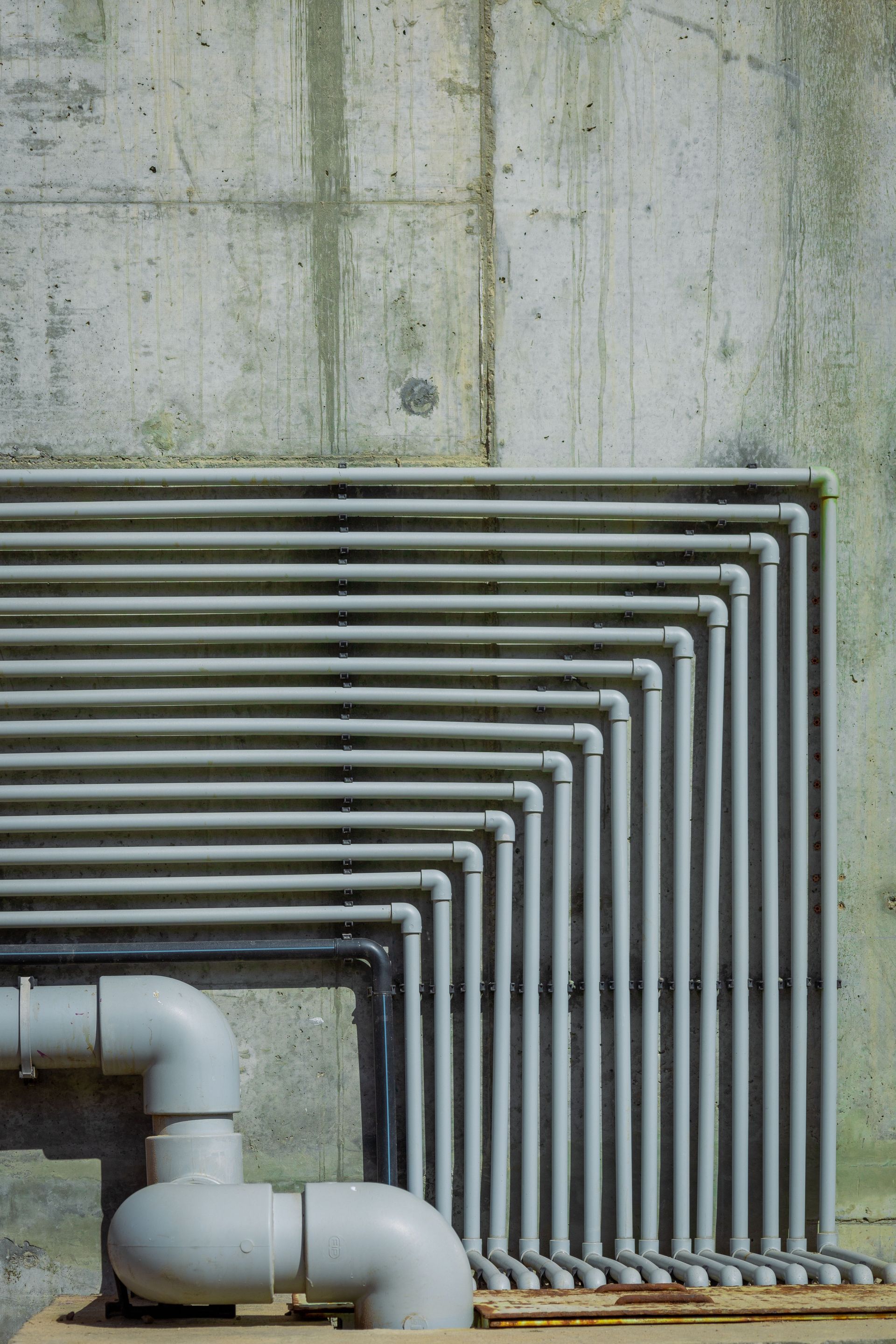 Close-up of industrial pipes against a textured concrete wall highlighting urban architecture.